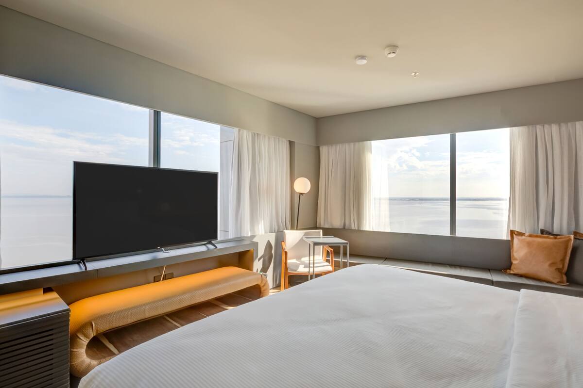 Une chambre d’hôtel moderne dotée d’un grand lit, d’une télévision à écran plat, d’un bureau et offrant une vue sur l’océan.
