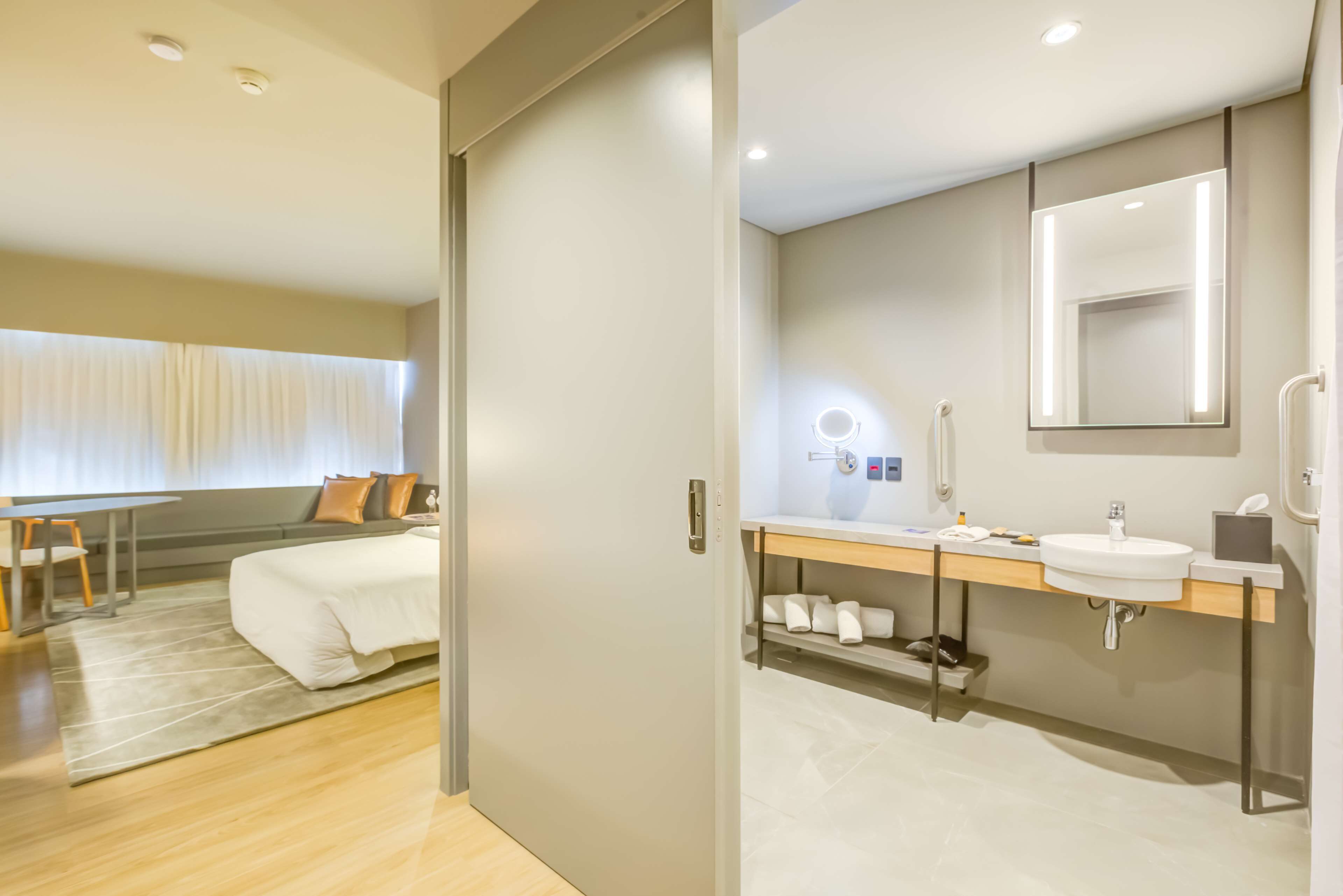 Een moderne hotelkamer met een bed, een bureau en een badkamer met een wastafel en spiegel.