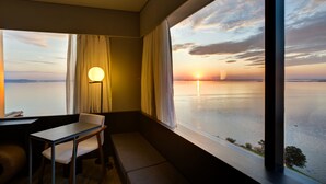 Una habitación con vista a un atardecer sobre el agua, una mesa, una silla y una lámpara.