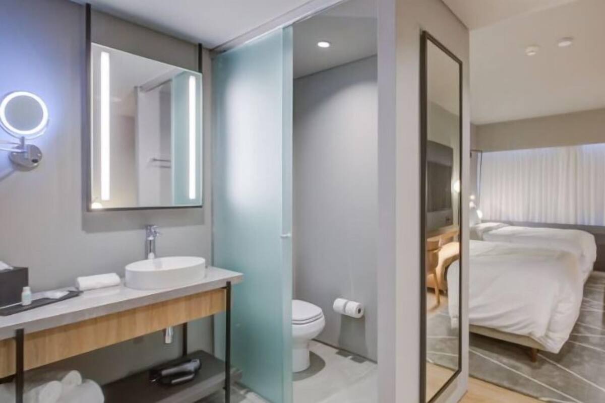 Une chambre d’hôtel moderne équipée d’une salle de bain, d’un lit, d’une télévision et d’un miroir.