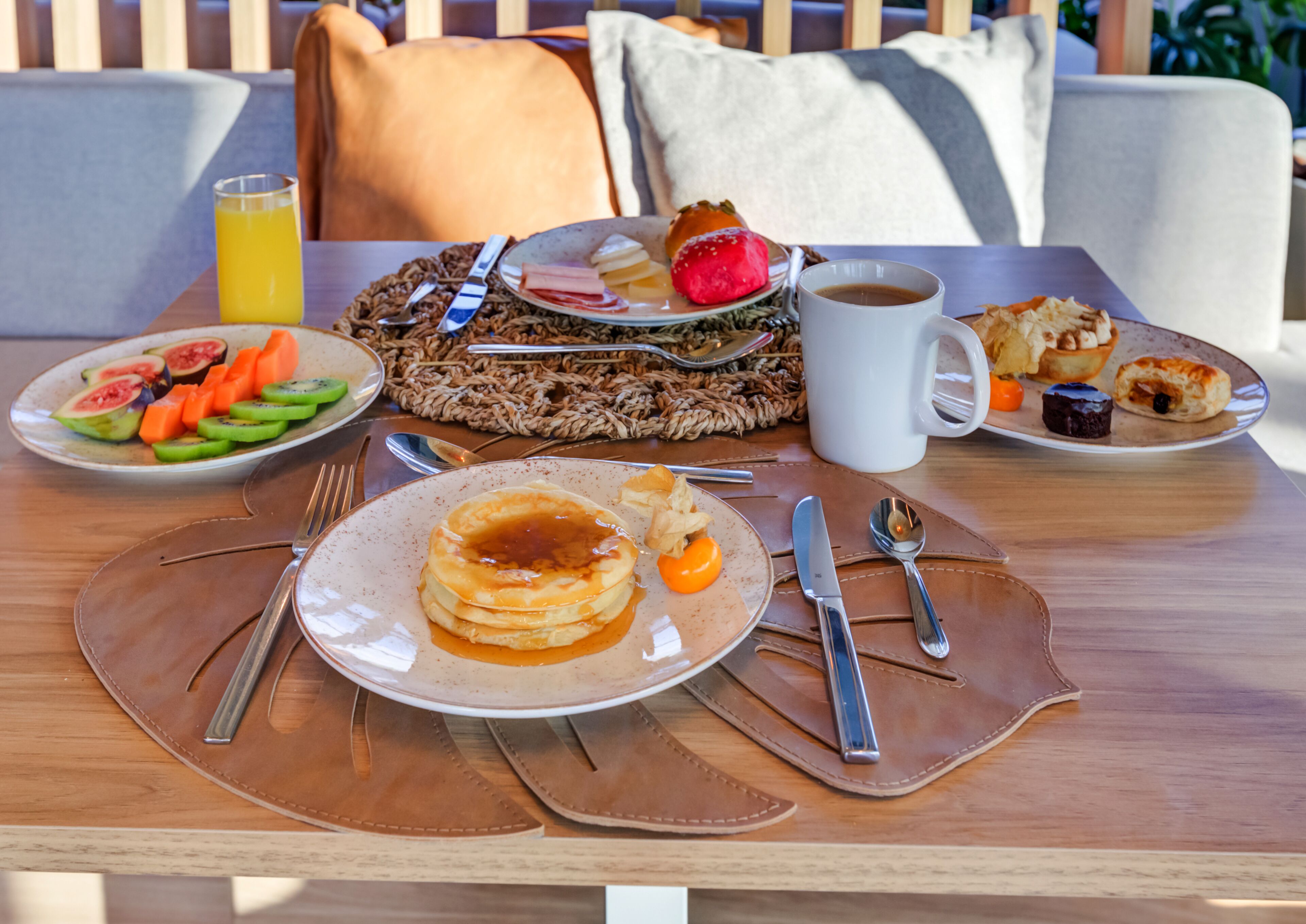 A breakfast table with pancakes, fruits, pastries, and a coffee cup.