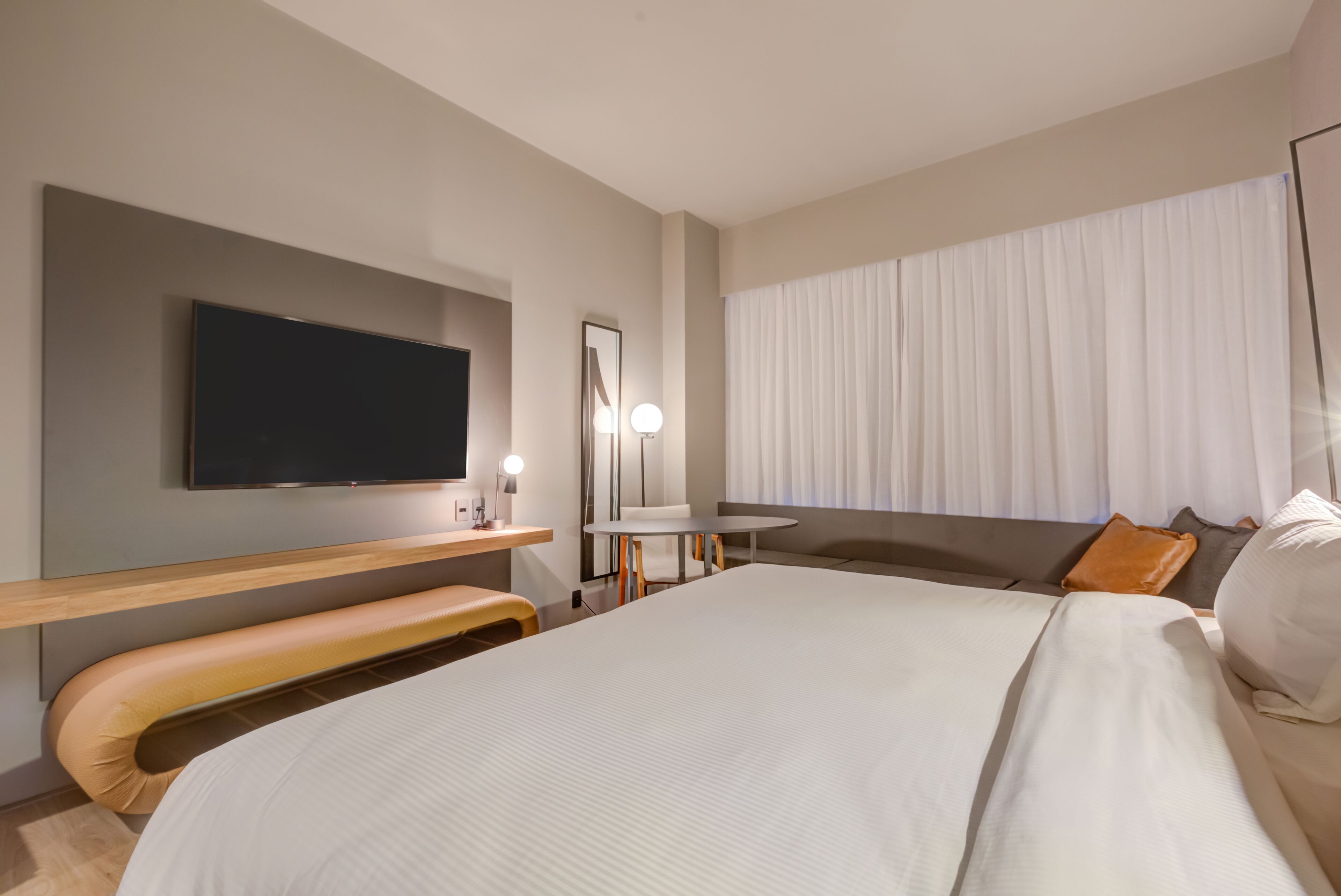 Een moderne hotelkamer met een groot bed, een flatscreen televisie, een bureau met een lamp en een raam met gordijnen.