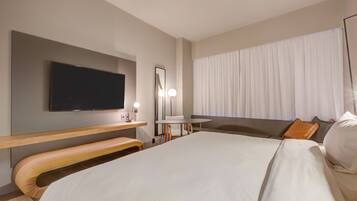 Een moderne hotelkamer met een groot bed, een flatscreen televisie, een bureau met een lamp en een raam met gordijnen.