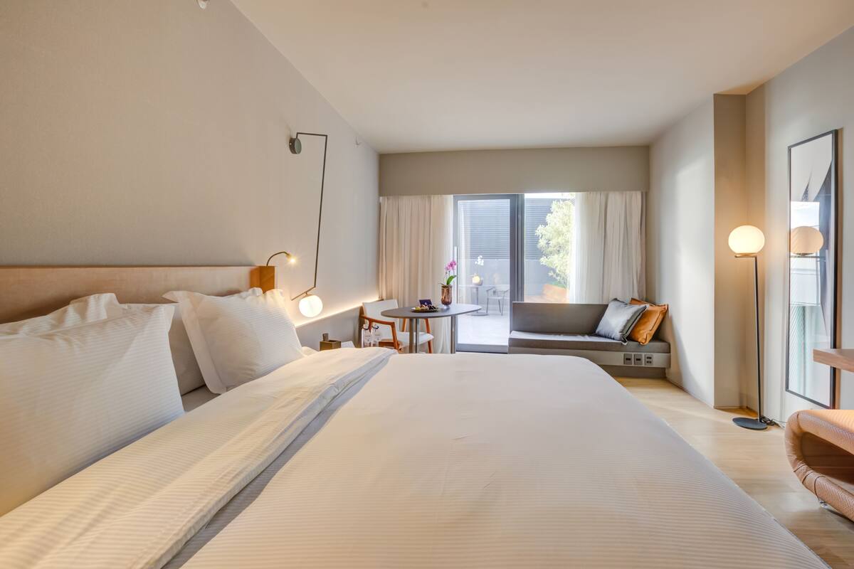 Une chambre d’hôtel avec un grand lit, une petite table, un canapé et un balcon avec des rideaux.
