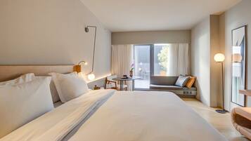 Quarto de hotel com uma cama grande, uma mesinha, um sofá e uma varanda com cortinas.