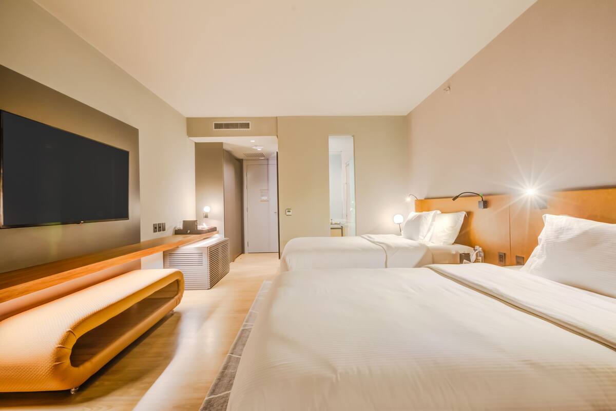 Une chambre d’hôtel avec un grand lit, une table de chevet, un téléviseur fixé au mur et une salle de bain visible à travers une porte ouverte.