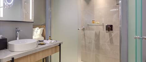 Un baño moderno con un lavamanos grande y redondo, un espejo con luz, ducha con mampara de vidrio y un perchero para toallas.