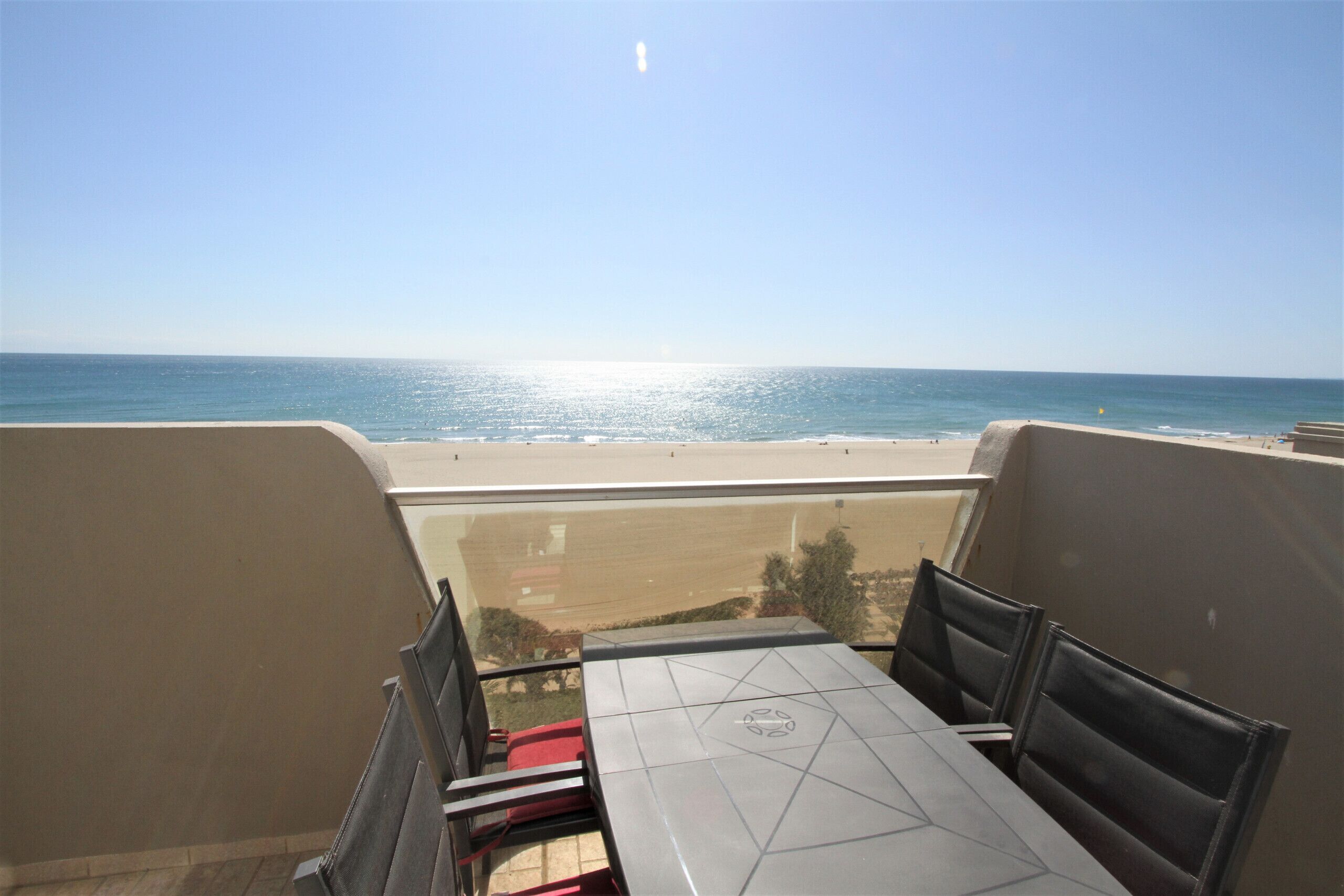 Un balcon avec une table et des chaises donnant sur une plage.