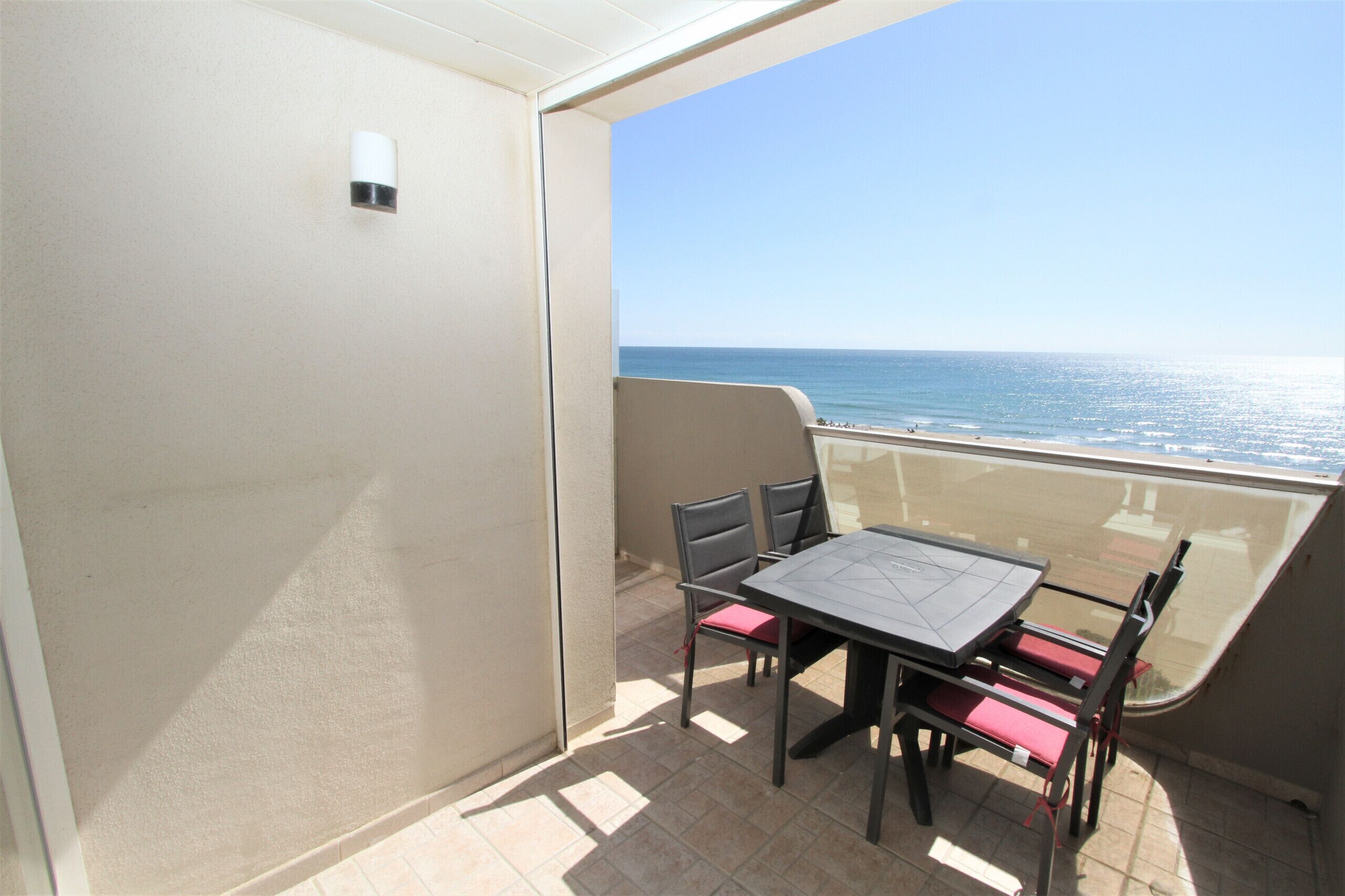 A balcony with a table and chairs, overlooking a beach.