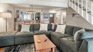 Ein modernes Wohnzimmer mit einem Ecksofa, einem Holztisch und einer Treppe, die in einen oberen Bereich führt.