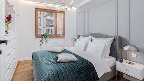 A bedroom with a bed, bedside table, lamp, and a window with a view of buildings. - EXCLUSIVE Aparthotel KRK Lubicz C4 with Garden (Kraków)