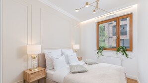 A bedroom with a bed, bedside lamps, a window with a view of a brick building, and a plant. - EXCLUSIVE Aparthotel KRK Lubicz C4 with Garden (Kraków)