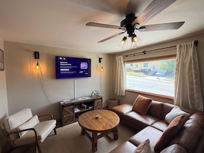 Un salon comprenant un canapé, une table basse en bois, un téléviseur fixé au mur et un ventilateur de plafond.