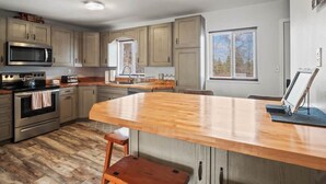 A kitchen with wooden cabinets, a stainless steel oven, a microwave, and a wooden island with stools. - 602 West 8th — 4BR Leadville Home, Hot Tub, Deck, Dogs OK, On the Mineral Belt (Leadville)