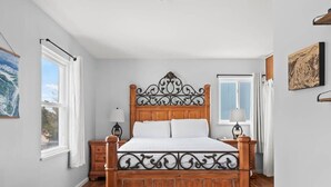 A bedroom with a wooden bed, two bedside tables, a window, and a painting on the wall. - 602 West 8th — 4BR Leadville Home, Hot Tub, Deck, Dogs OK, On the Mineral Belt (Leadville)