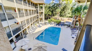 Ein Poolbereich eines Hotels mit mehreren Balkonebenen, Liegestühlen und Sonnenschirmen.