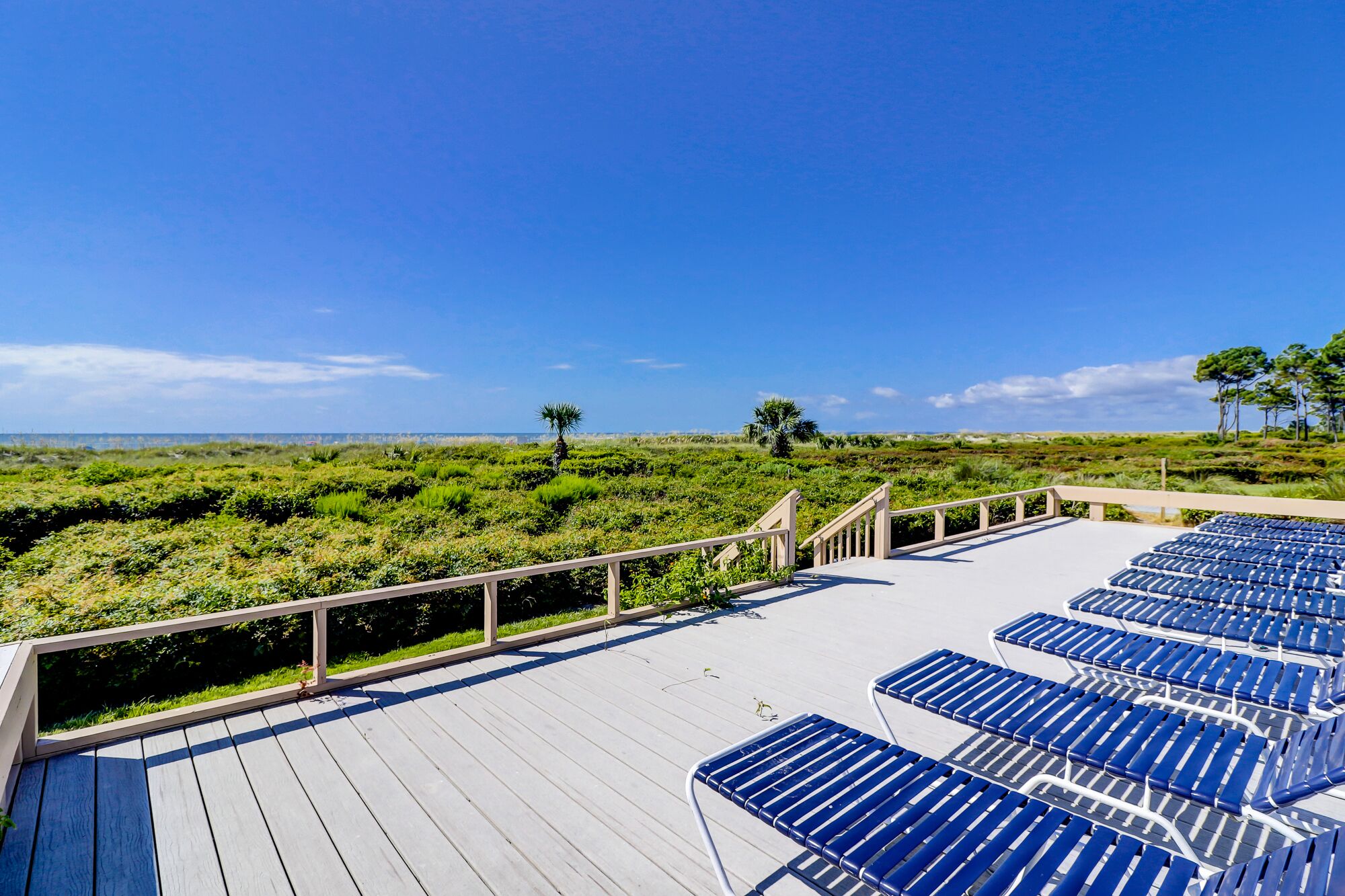 A deck with blue lounge chairs, a wooden pathway, and a view of a coastal landscape.