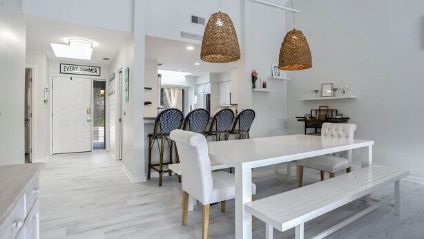 Una cocina moderna con armarios blancos, un comedor con mesa y sillas blancas, y lámparas colgantes de fibra.