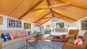 Een knus loft-achtig vertrek met een hoge plafond, een bank, een stoel en een eethoekje.