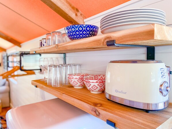 Un coin cuisine avec des étagères en bois où sont rangés divers ustensiles, notamment des assiettes, des bols et un grille-pain.