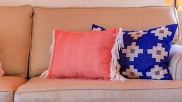 Un sofá beige con dos almohadones decorativos, uno rojo y otro azul con estampado geométrico, y dos obras de arte abstracto en blanco y negro en la pared de arriba.
