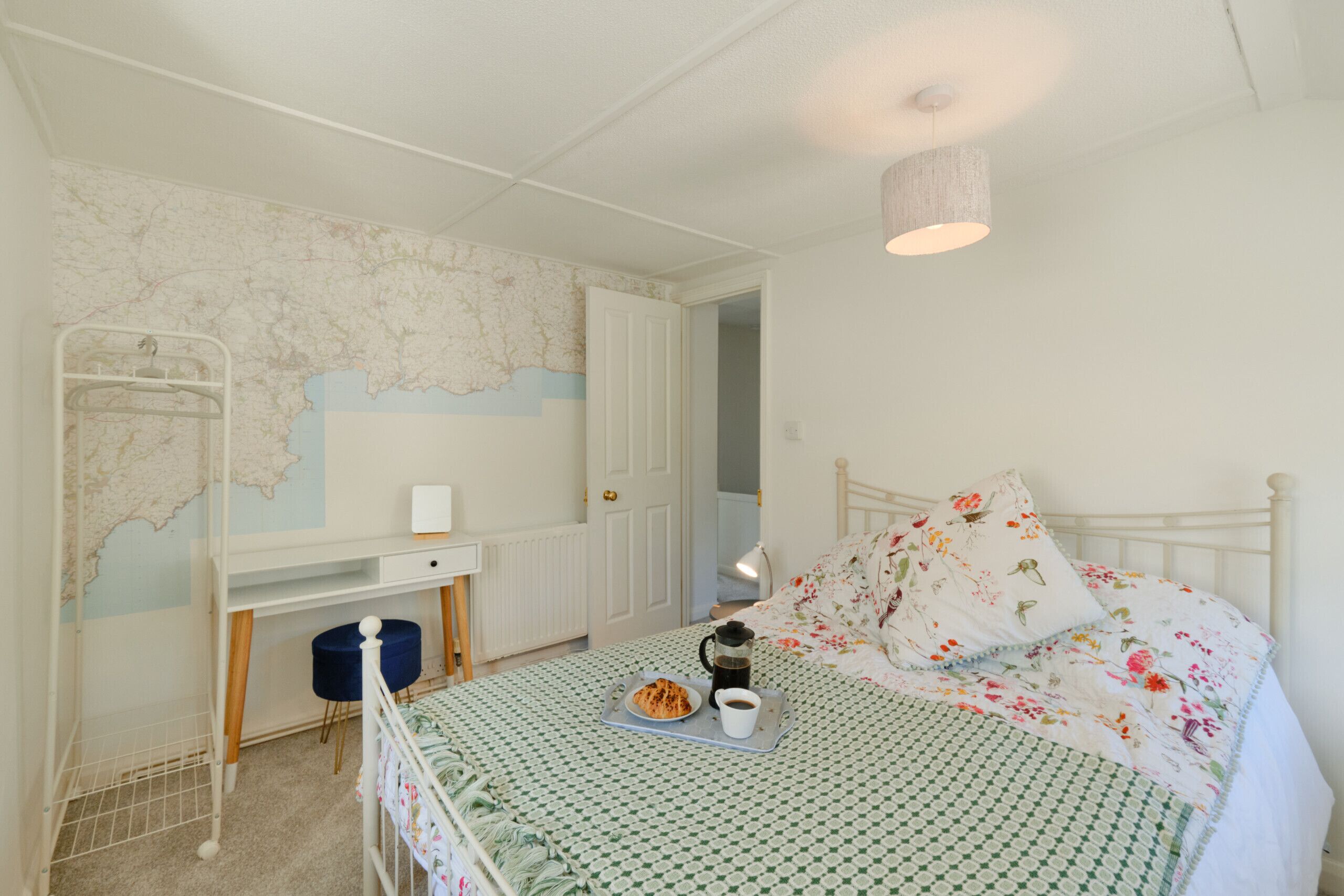 Una camera da letto con un letto a castello, una scrivania, una mappa appesa al muro e un vassoio per la colazione sul letto.