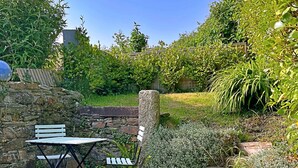 Eine Terrasse mit Tisch und Stühlen, umgeben von Steinmauern und üppiger Bepflanzung.