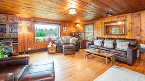 A cozy cabin interior with wooden walls and floors, featuring a leather sofa, a recliner, and a coffee table.