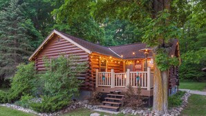 A log cabin with a porch, steps, and string lights.