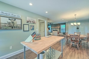 Un comedor con una mesa y sillas de madera, un letrero que dice "Backyard Burger Spot" y una cocina al fondo.