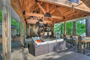 A covered outdoor seating area with a sofa and tables, surrounded by wooden beams and a view of trees. - Lakefront Retreat w/ Deep Water + Great Views! (Eatonton)