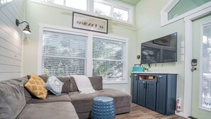 A cozy living room with a sectional sofa, a blue ottoman, and a TV mounted above a dark blue cabinet.