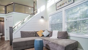 A modern living room with a gray sectional sofa, a blue ottoman, and a staircase with wooden railings.