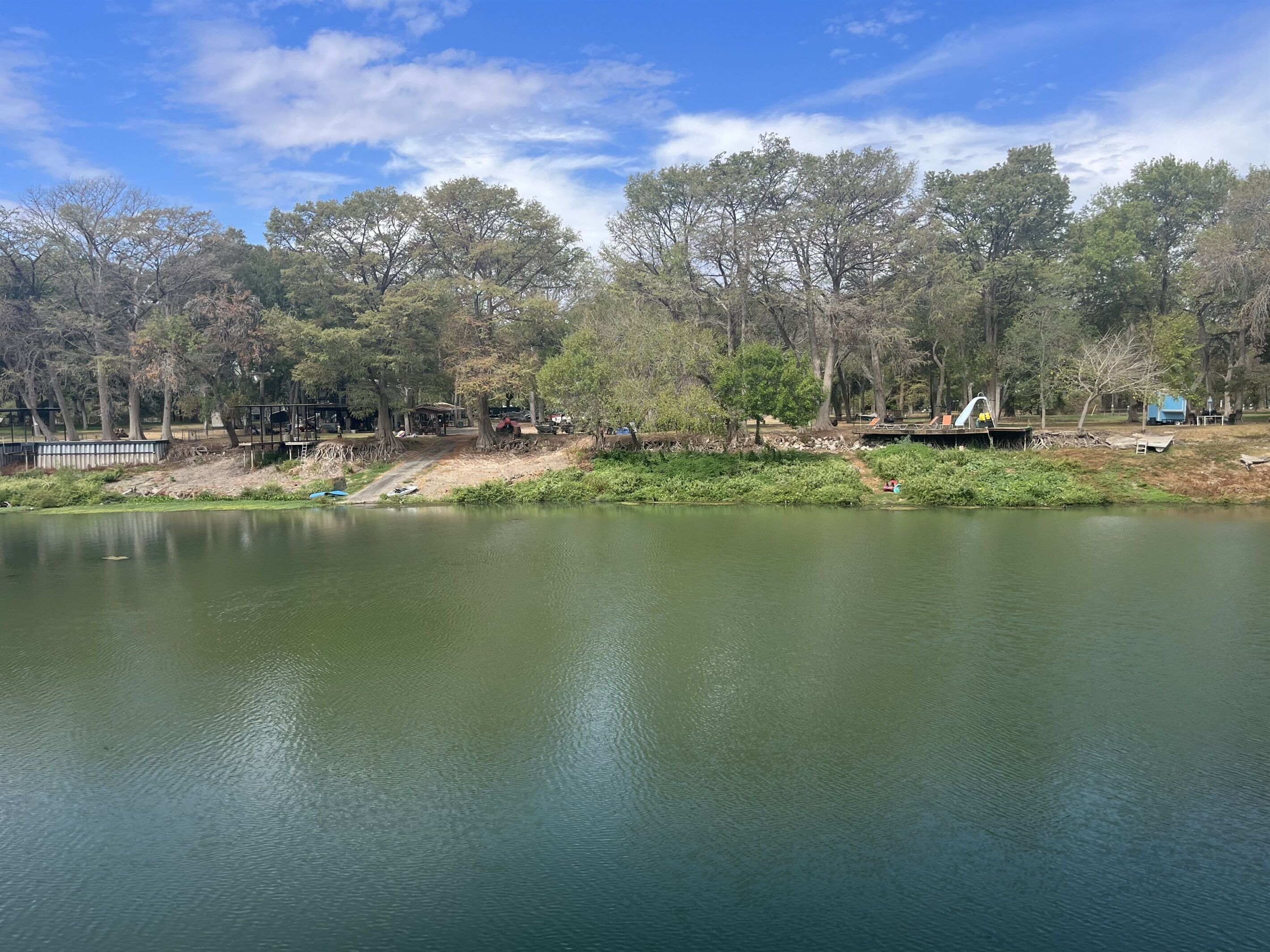 A serene lakeside park with trees, a dock, and a small bridge.