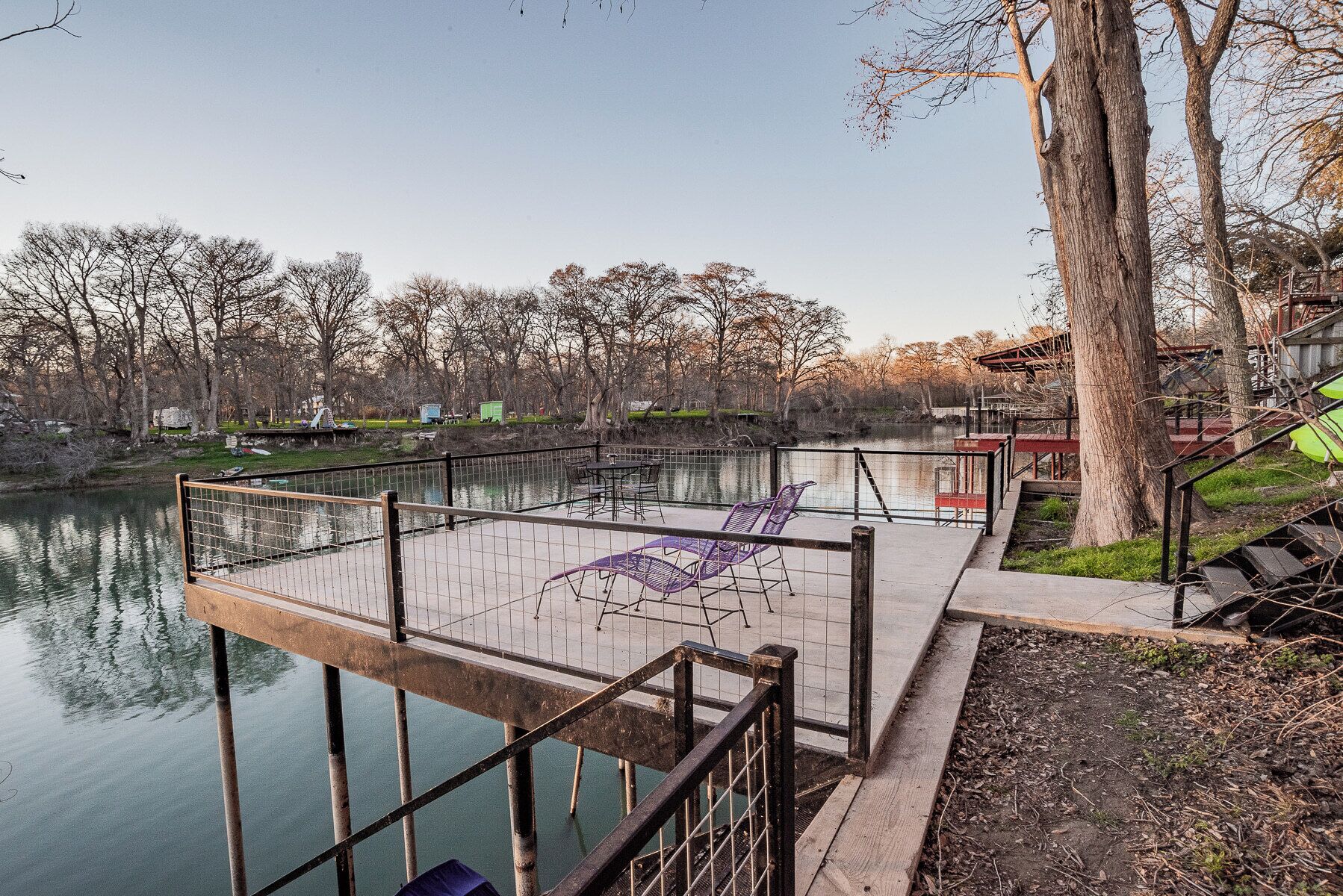 A wooden dock extending over a calm lake, with metal railings and chairs for seating.
