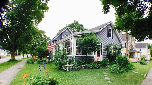 A residential house with a front porch, a small garden with flowers, and an American flag.