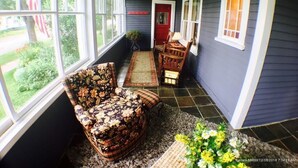 A covered porch with a floral-patterned chair, a small table, and a red door.