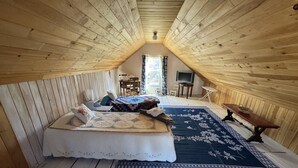 A loft bedroom with a sloped ceiling, a bed, a TV, a small table, and a window with curtains.