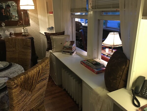 A cozy room with a sofa, a small table with books, a lamp, and a window with blinds.