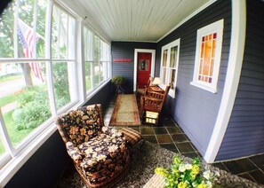 A covered porch with a floral-patterned chair, a small table, and a red door.