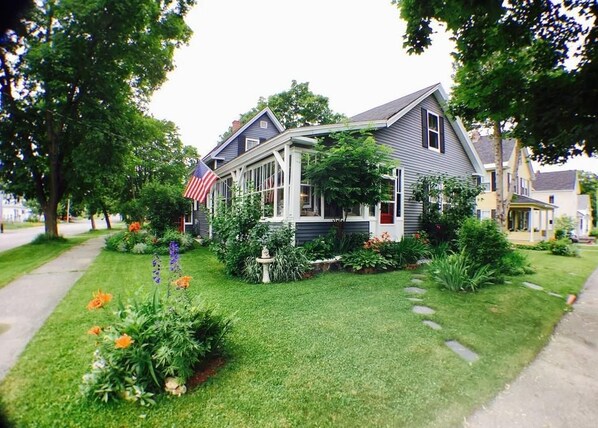 A residential house with a front porch, a small garden with flowers, and an American flag.