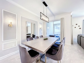 A modern dining room with a long table, multiple chairs, and a chandelier.