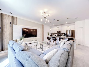 Een moderne woonkamer met een grote flatscreen televisie, een bank en een eethoek met barstoelen.