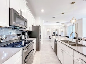 Een moderne keuken met roestvrijstalen apparatuur, witte kasten en een centraal eiland met een spoelbak en zitplaatsen.