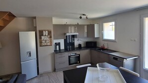 Een moderne keuken met een koelkast, magnetron, fornuis en gootsteen. Er hangt een houten bord aan de muur en een raam zorgt voor natuurlijk licht.
