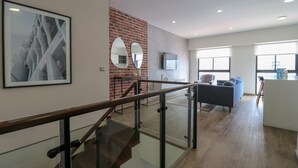 A modern interior with a staircase, a brick wall, a living area with a sofa and TV, and a large framed artwork.