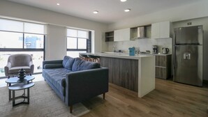 A modern apartment with a living area, kitchenette, and a balcony with a city view.