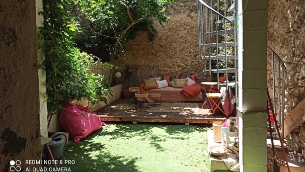 Zona d'estar a l'exterior acollidora amb sofà, coixins i taula petita, envoltada de vegetació i un mur de pedra.