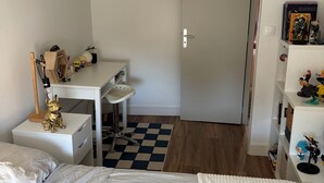 Un dormitori amb un llit, un escriptori i una cadira. Hi ha una porta que condueix a una altra habitació.