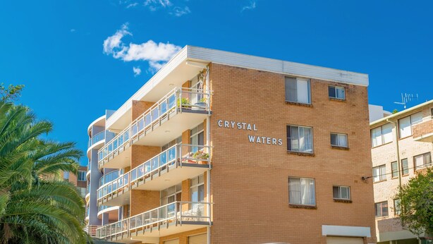 En flervåningsbyggnad med balkonger, en klar himmel och namnet ”CRYSTAL WATERS” skrivet på sidan.